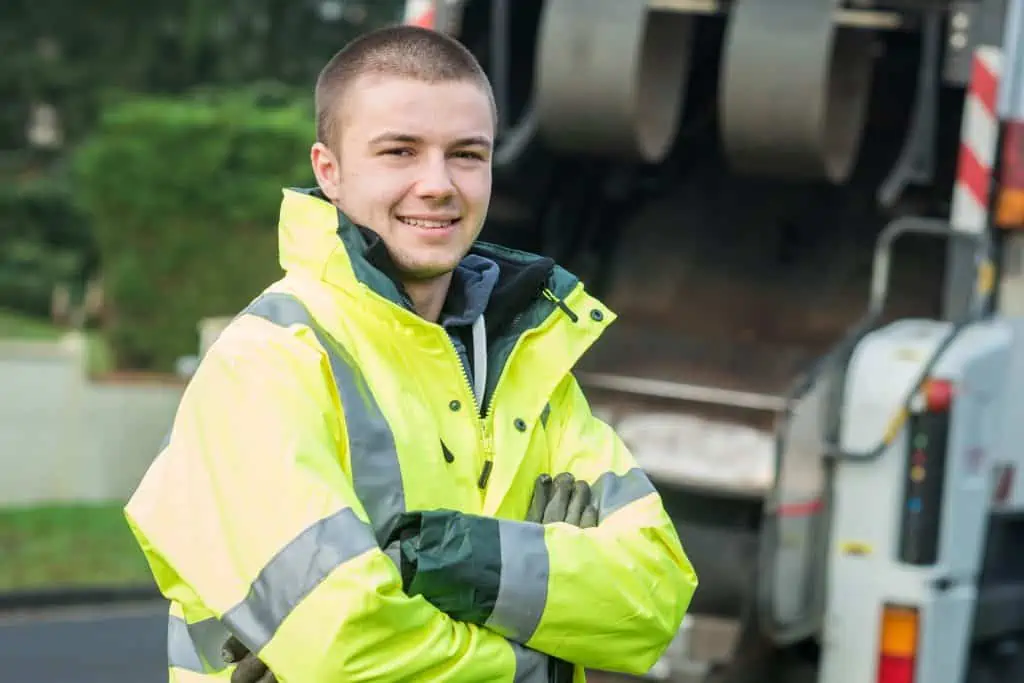 Do sign on bonuses work? Young garbage worker with safety coat smiling in front of garbage truck
