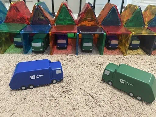 Toy waste trucks blue and green with Inflection Poynt on the side. Parking in magnetic tile garages
