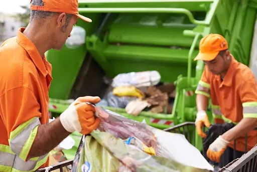 Workers loading bags of trash into a garbage truck.