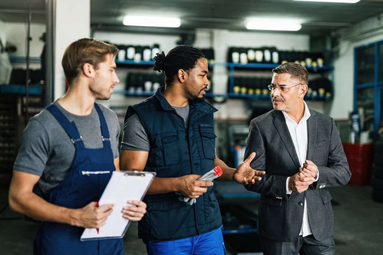 African American auto mechanic and his coworker communicating with their manager in repair shop.