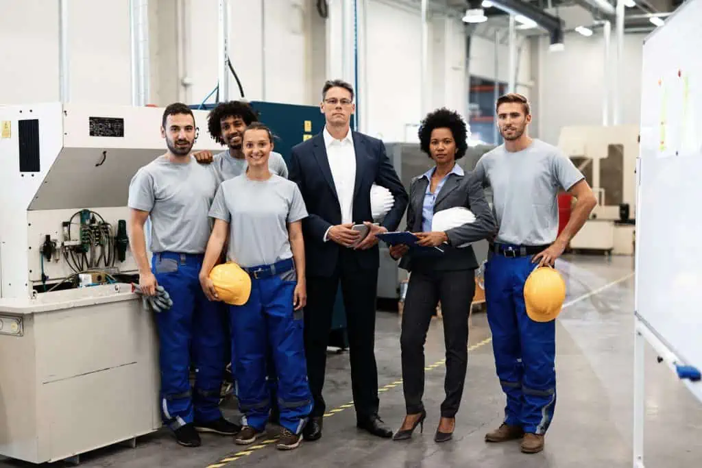 Portrait of group of engineers and corporate managers standing in a factory and looking at camera.