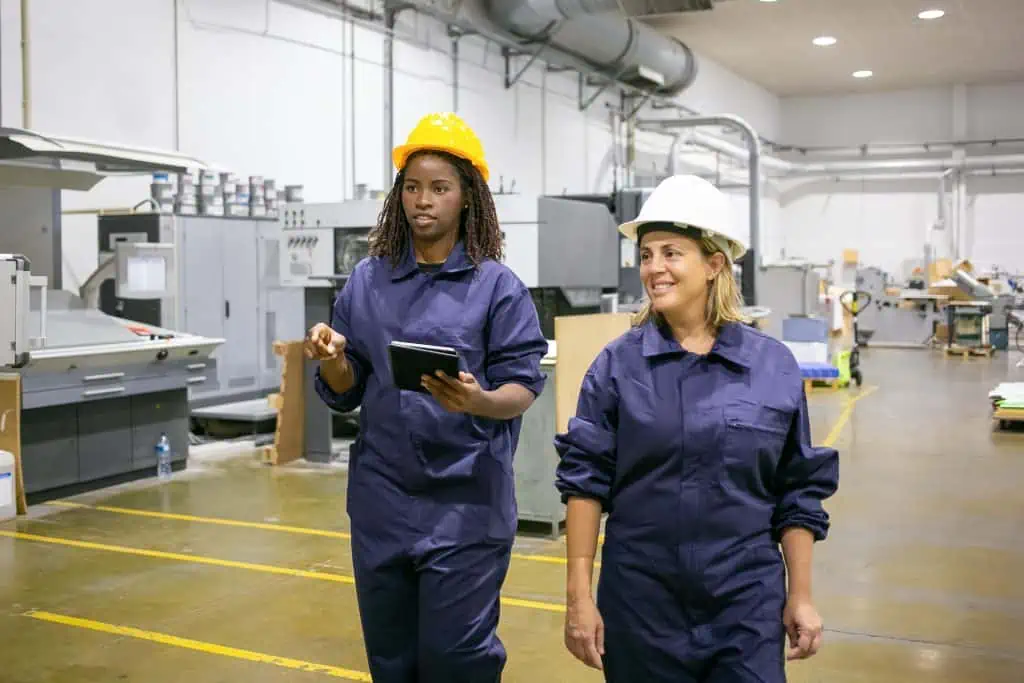 Two women in a warehouse wearing safety equipment.