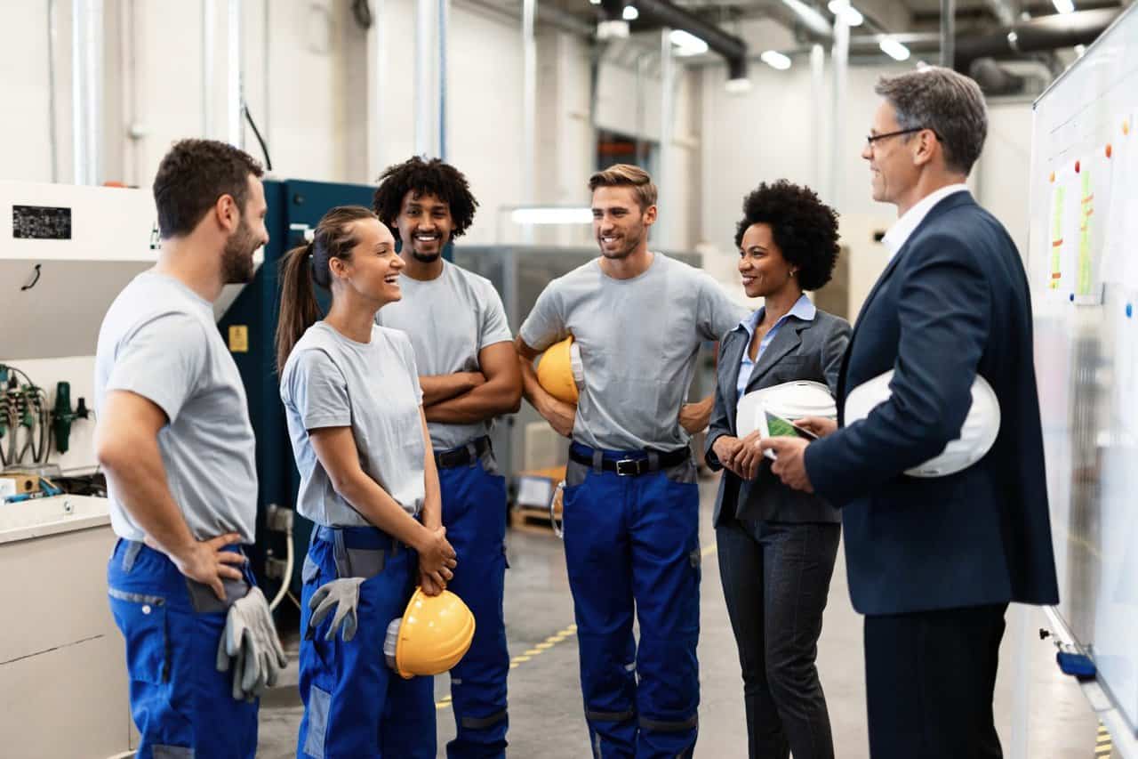 Young happy female worker and her colleagues communicating with company managers in a factory.