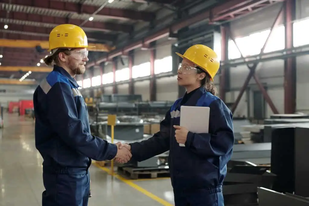 Confident industrial colleagues in workwear and protective goggles making handshake in workshop after reached agreement