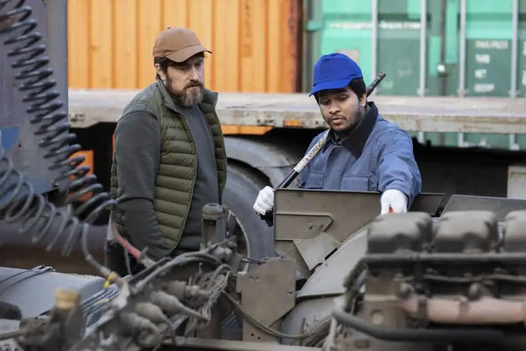 Two men looking at the engine compartment of a truck.