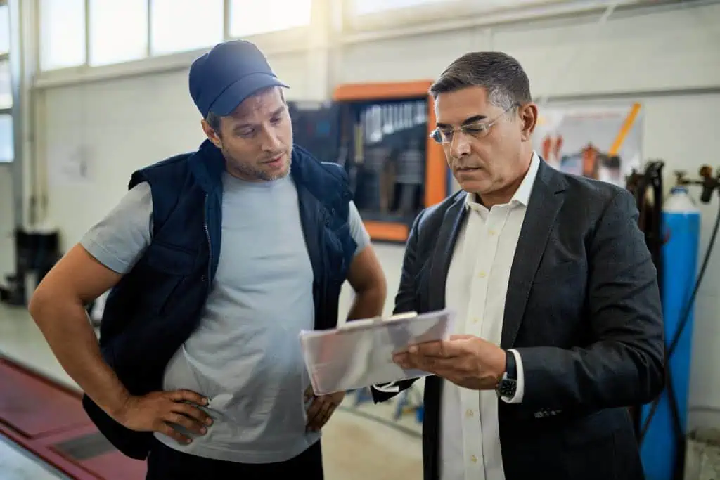 Mid adult manager and car mechanic analyzing data while going trough reports in auto repair shop.