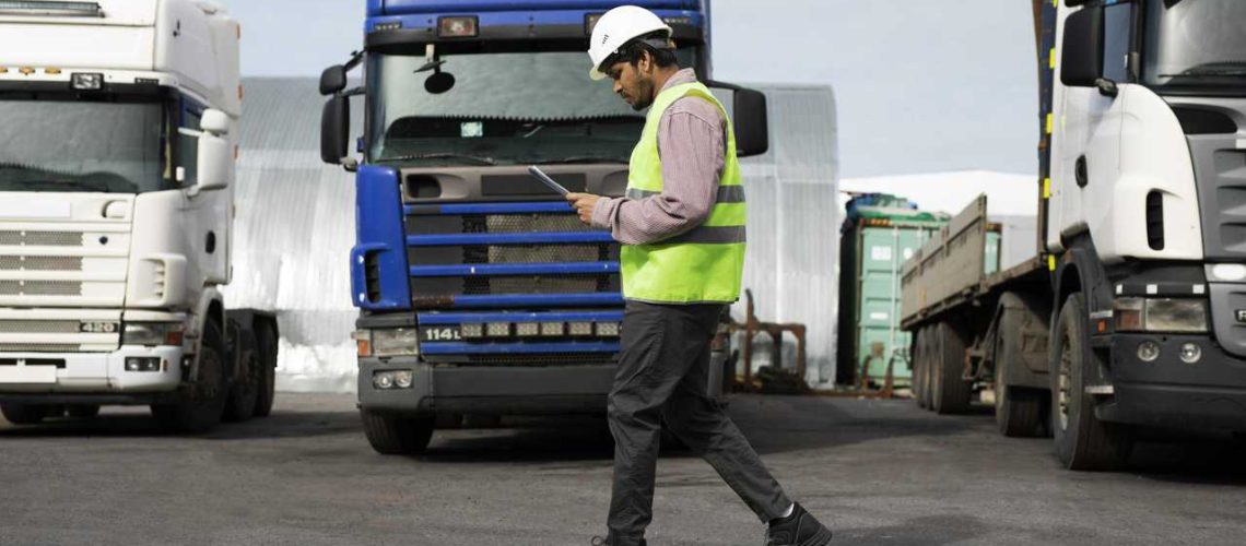 Man looking at papers walking in front of a row of trucks.