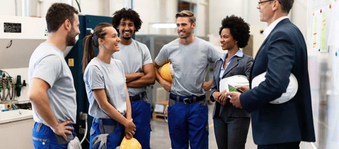 Young happy female worker and her colleagues communicating with company managers in a factory.